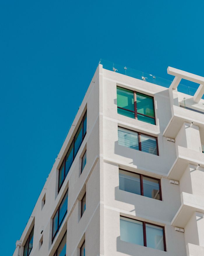 services-04 A modern white high-rise building against a clear blue sky, architectural design with large windows.